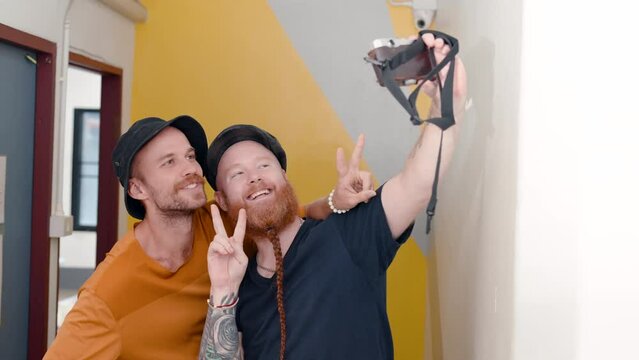 4K, Two male tourists who are best friends are standing at counter in hostel's living room. Both them are taking selfies themselves, When finished shooting, you can scroll through images from camera.