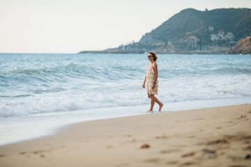 The girl walks along the shore along the sea at sunset.