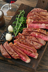 Steaks. Sliced grilled meat steak New York or Ribeye with spices rosemary and pepper on black marble board on old wooden background. Top view. Mock up.