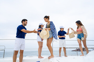Man and woman yacht crew in uniform helping group of passenger tourist get on luxury private catamaran boat yacht to sailing in the ocean on summer vacation. Cruise ship service occupation concept. - obrazy, fototapety, plakaty