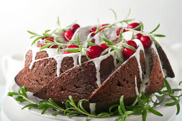 Christmas chocolate bundt cake. Traditional Christmas fruit cake with white glaze, cranberries and rosemary on white stand with Christmas decoration. Winter baking at Xmas or New Year. Copy space.