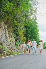 Cheerful, happy family, father, mother, son and daughter enjoying walk play outdoor near sea. Funny family in white clothes barefoot running on walkway. Green rocks at background.