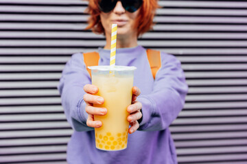 Glass of fruity sugar flavored tapioca pearl bubble tea with straw in hand of hipster fashion woman...