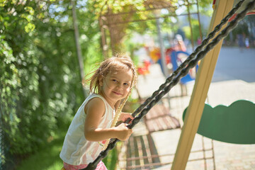 A child on a swing is playing on an outdoor playground. An active child is swinging on a swing. Healthy summer activity for children. A little girl in the fresh air..