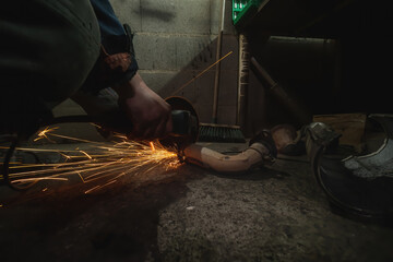 Pipe cutting, sparks fly. Car service. On the ground in a pit. Man repairing of corrugation muffler catalyst of exhaust system in car workshop - mechanic cleans the muffler pipe by angle grinder