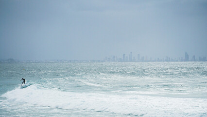 Surfing in a foggy day with The Gold Coast behind with its buildings and skyscrapers behind