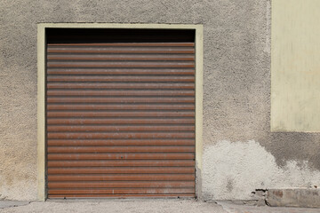 Old cracked housewall with brown closed garage door, gate with roll up jalousie