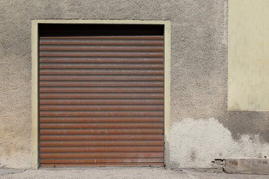 Old cracked housewall with brown closed garage door, gate with roll up jalousie