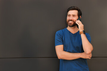 Happy man talking on phone near grey wall. Space for text