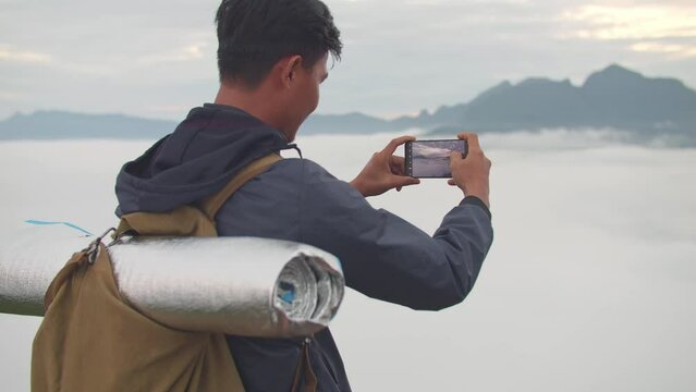 Asian Hiker Male Using Smartphone Taking Photo Of The Top View Foggy Mountain

