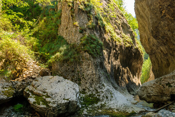 A mountain stream flowing through a canyon narrowed by vertical stone walls. The sharp, rocky cliffs of Ramet Gorges or Cheile Rametului ( Romania) during summer season in a sunny day. Natural tunnel