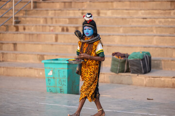 Portrait of a young boy dress up like lord shiva with painted blue face near river ganges ghat in varanasi city.