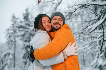 Lovely couple embracing each other while standing in the winter forest