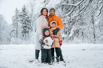 Fototapeta na wymiar Happy family is standing in the winter forest together. Parents with kids