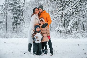 Happy family is standing in the winter forest together. Parents with kids