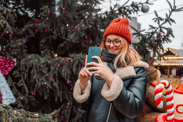 Happy blonde woman takes a picture of a European Christmas market with a smartphone. The girl...