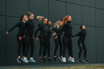 Jumping together. Group of sportive women is outdoors near black building