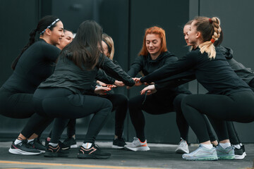 Conception of teamwork. Group of sportive women is outdoors near black building