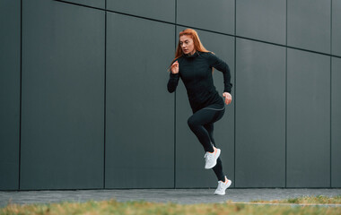Woman is sportive clothes is running outdoors against black building