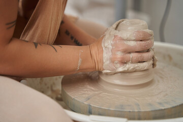 Close-up view of a woman modelling clay on potters wheel in a ceramic workshop. Craft, art and hobbies concept.