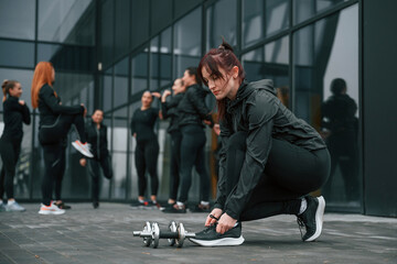 Ties shoelaces. Group of sportive women is outdoors near black building