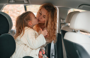 Little girl is sitting in the car. Mother is taking care of her daughter