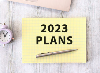2023 PLANS text written in a notebook lying on a wooden work table next to a laptop