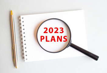 The magnifying glass rests on the pad and shows 2023 PLANS on a white page. There is a pen next to it.