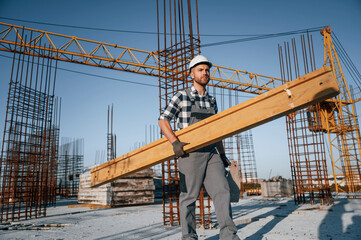 Moving wooden plank. Man is working on the construction site at daytime