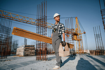 With toolbox and wooden plank. Man is working on the construction site at daytime