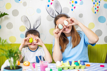 Mother and her son holding colorful Easter eggs in front of eyes