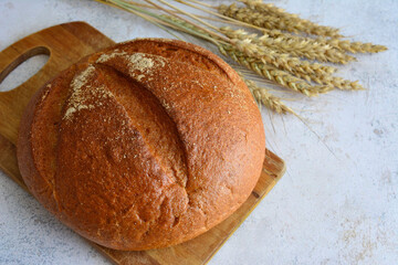 round rye bread isolated on cutting board and decorated with ears of wheat, macro