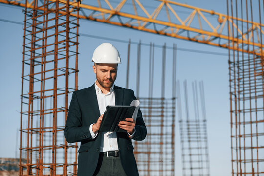 Standing and holding digital tablet. Businessman in formal clothes is on the construction site at daytime
