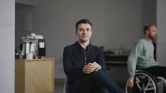 Portrait young caucasian disabled man with silicone prosthesis hand sitting indoors, artificial limb. Wheelchair man on background. People with physical disability, inclusion and inclusiveness concept