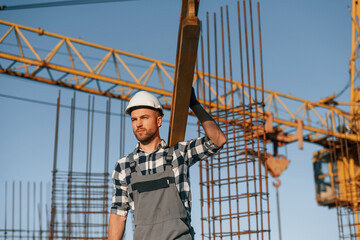 Against crane. With wooden plank. Man is working on the construction site at daytime