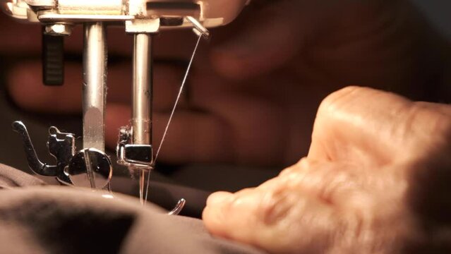Hands working sewing machine in motion. close-up of sewing machine needle quickly moves up and down. Old woman working. The process of sewing the fabric.

