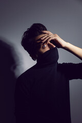 Fashion Portrait of a 35 year old man standing over a light gray background in a black sweater covers his face and mouth with clothes. blue eyes and hair up. Close up. Studio shot