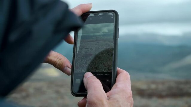 Close-up of man photographing mountain landscape with man. Clip. Phone screen is in hands of man photographing mountain landscape. Man takes pictures on phone of man in mountains