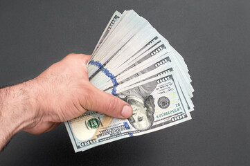 Hand holding one hundred dollar bills against black background. - 556514890
