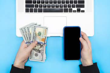Laptop, smartphone and money in male hands, top view.