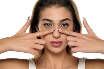 Fototapeta premium young woman touches her nose with her finger on a white background. Front view.