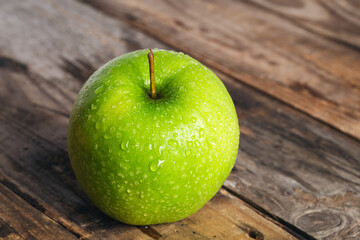 Green apple with water drops on a wooden background close-up.