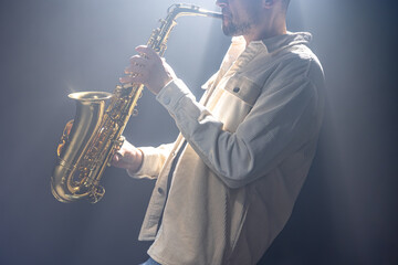 A European man plays the saxophone in the dark.
