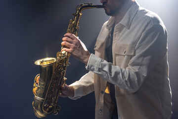 Naklejka na ściany i meble Male musician on stage plays the saxophone dark with smoke.