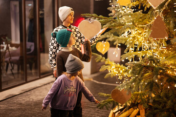 Three kids having fun near illuminated Christmas tree outdoor in evening.