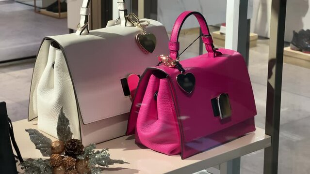 Women's white and pink leather handbags stand on a shelf in the showcase of an accessories store.