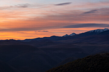 Dark silhouettes of mountains against a bright orange sunset sky. Red sunset over majestic mountains. Sunset in magenta tones. Atmospheric purple landscape with a high-altitude snowy mountain valley.