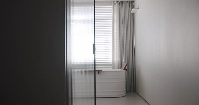 Transparent sliding door opens inside the modern bathroom, minimalist bathtub in white and gray colors. Modern Minimalist white bathroom.