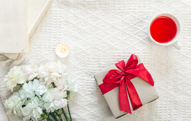 Gift box, flowers and a cup of tea in bed, top view.