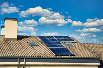 Solar panels on the roof of some houses with cloudy blue sky in the background.